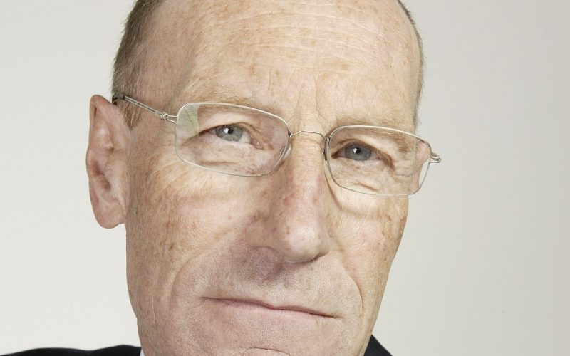 Sir John Armitt wearing a dark suit, white shirt and pale green tie.