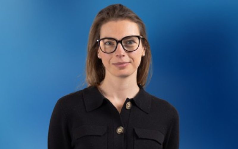 Louise Evans wearing glasses and a black shirt against a blue background.