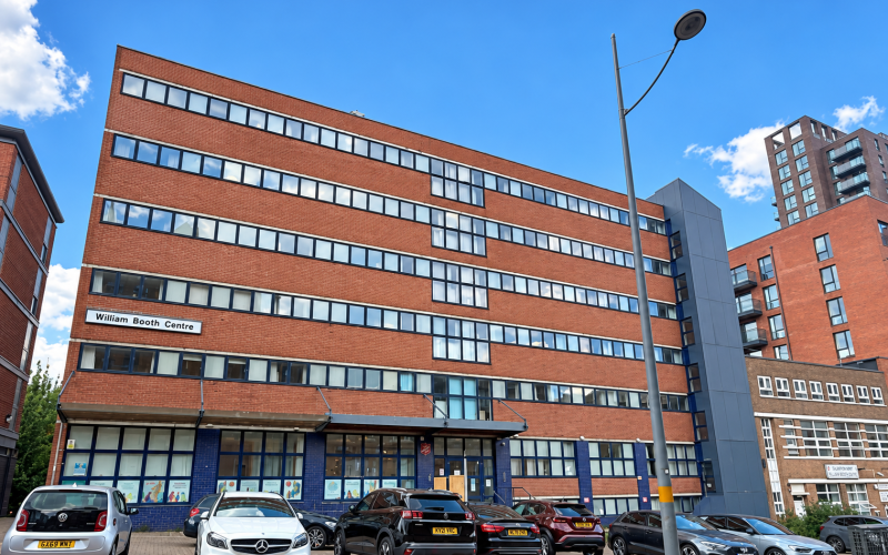 Illustration of the William Booth Centre on Shadwell Street, a brick multi-storey building beside parked cars.