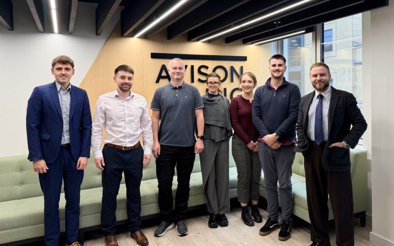 Eight Avison Young colleagues stand together in a Leeds office meeting room.