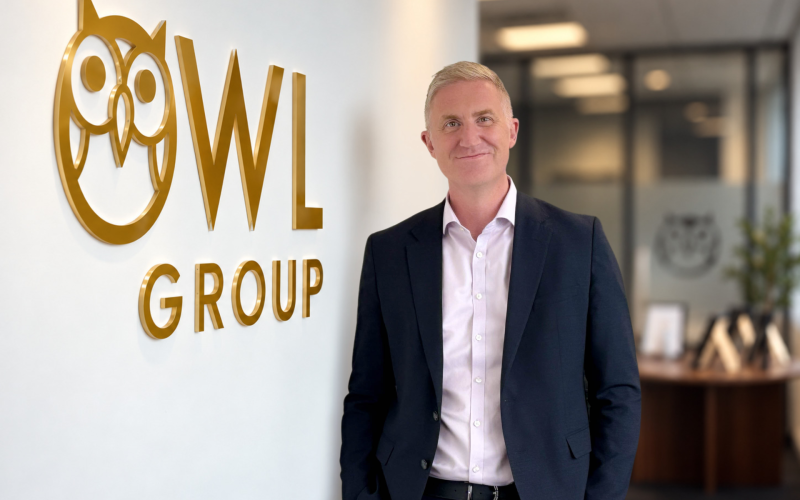 Steve Breslin stands beside an Owl Group logo in a suit.