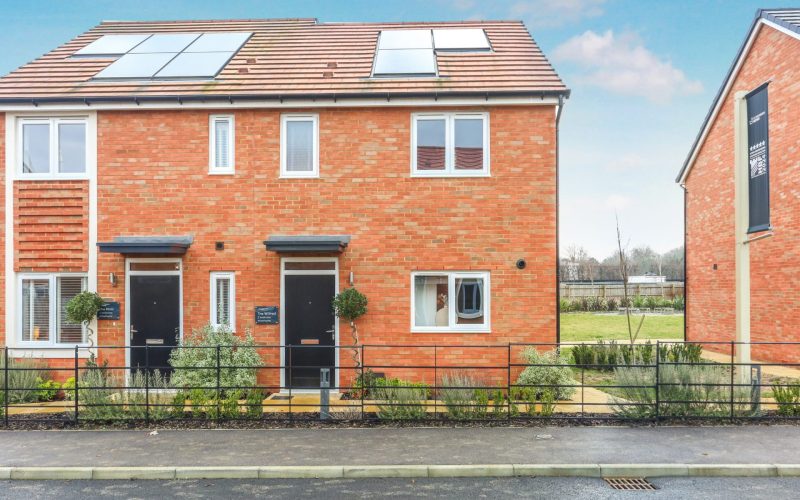 Newly built brick terraced homes with solar panels, front gardens and a paved street