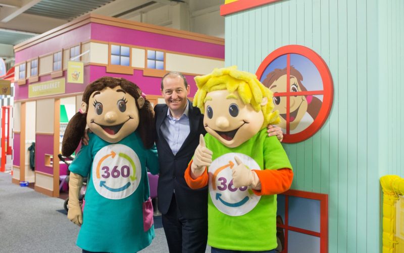 Two 360° mascots pose with a smiling man inside a brightly coloured children’s play area.