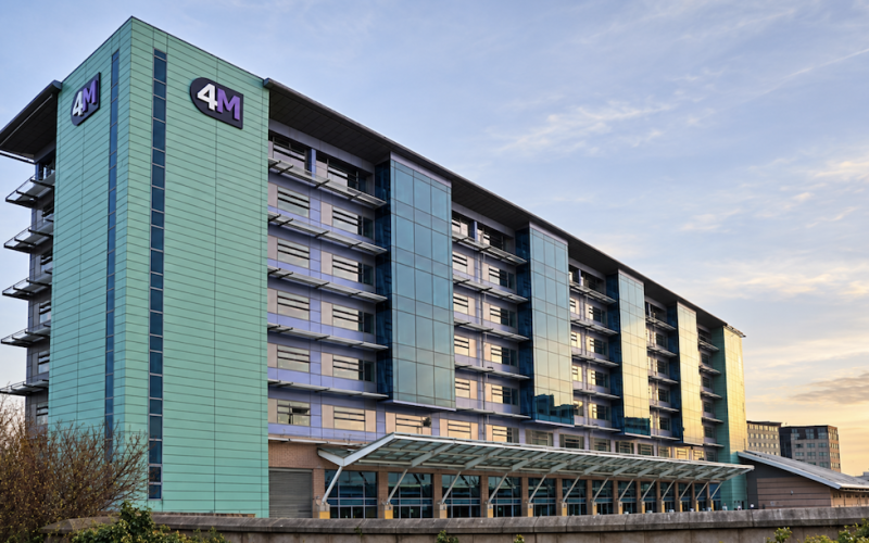 Exterior of the 4M Manchester Airport office building, a multistory green-glass building above the transport interchange.