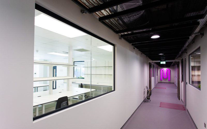 Modern office corridor with glass meeting rooms and a glowing pink wall logo