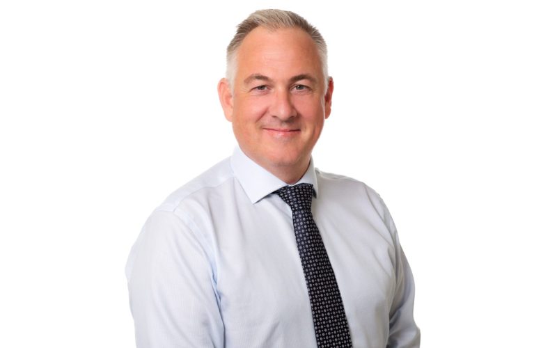 Shaun Dawson, wearing a white shirt and dark tie, smiles at the camera.