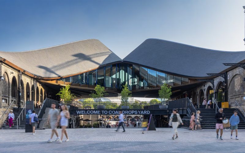 Pedestrians walk past the entrance to Coal Drops Yard, with its sign beneath the glass roof.