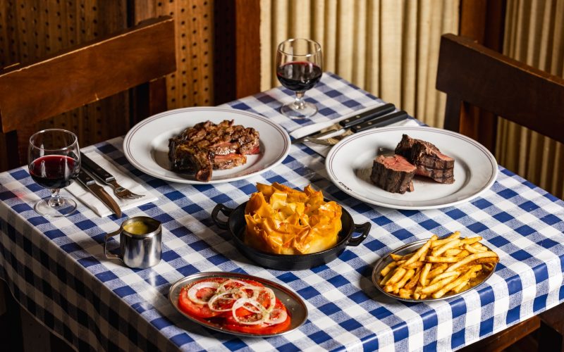 Illustration of a blue-and-white checked tablecloth set with several South American-inspired dishes and drinks.