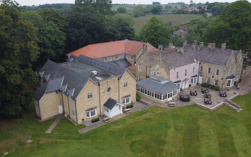 Aerial view of the Hall Garth Hotel, a cluster of connected buildings surrounded by lawns and trees.