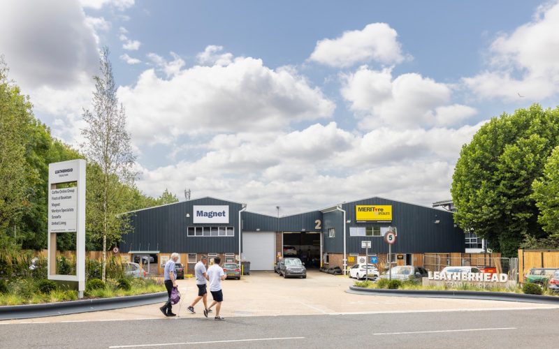 People walk past refurbished industrial units at a landscaped logistics estate under a cloudy sky