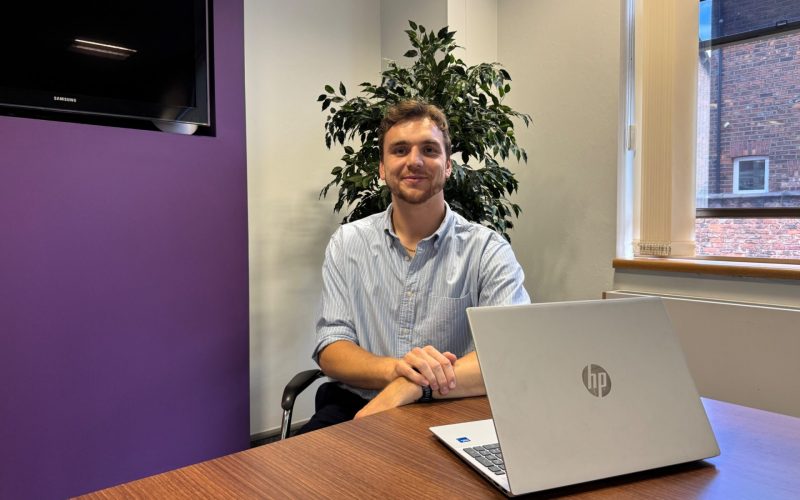 Joe Cooke sits at a desk with a laptop in an office.