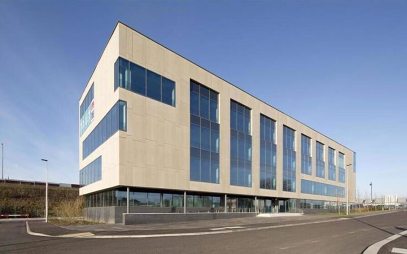 A modern office building with a cream coloured facade and lots of windows down the side of the building