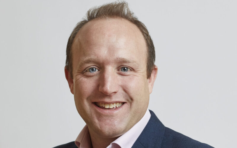 A smiling man wearing a dark suit jacket and a light coloured shirt