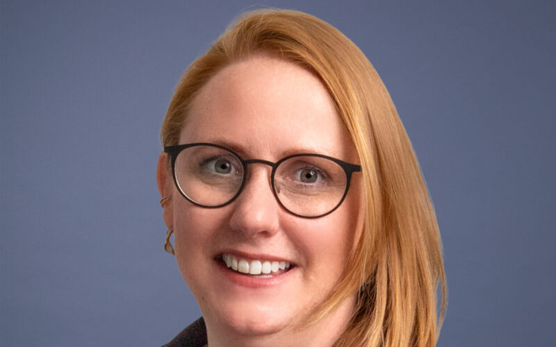 A smiling woman with long hair wearing glasses
