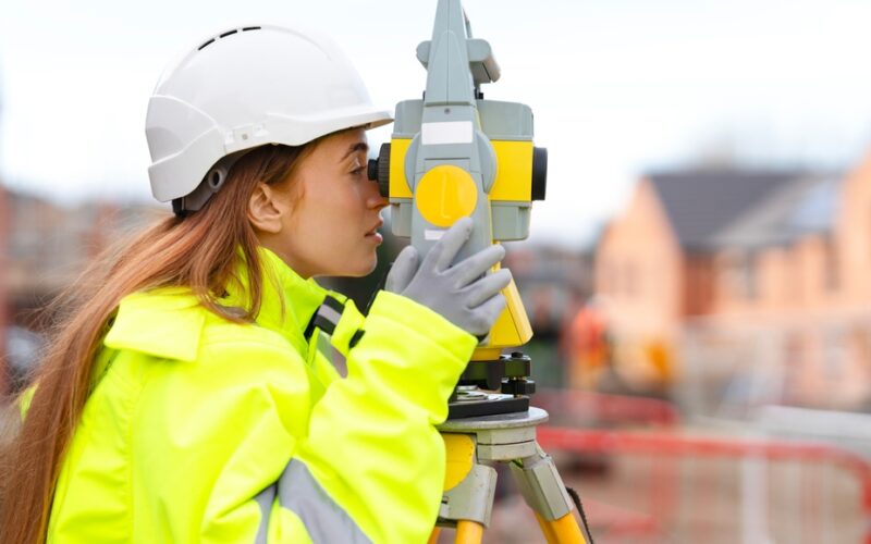 Portrait,Of,Young,Woman,In,Safety,Gear,Using,A,Surveying