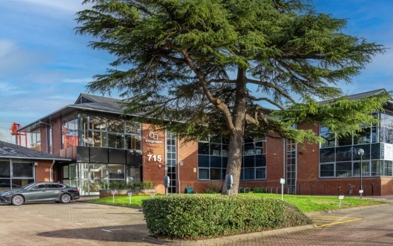 A brick built office building with a large tree and hedge in front