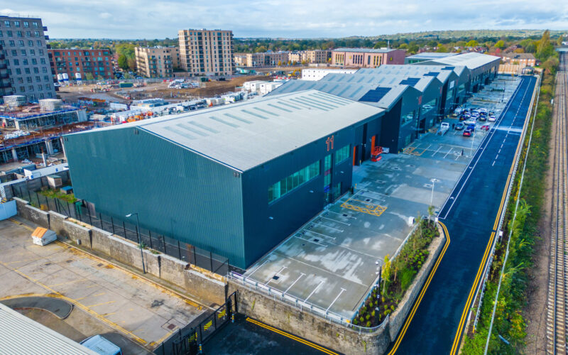 Aerial view of a row of blue industrial buildings with a development site in the background