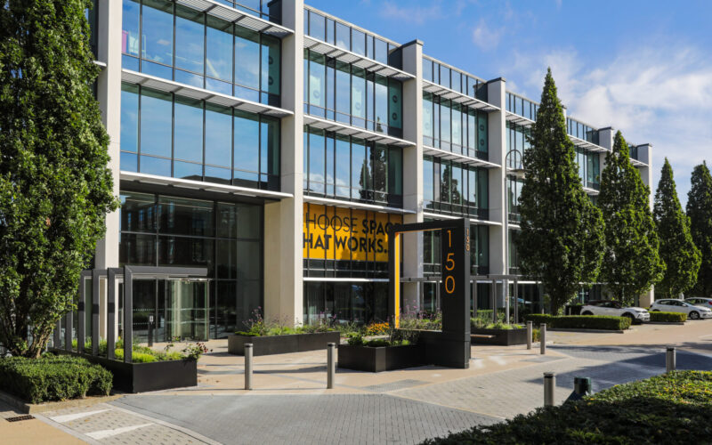 Exterior of a modern low-rise office building featuring lots of glass windows along the facade with trees and landscaping in the foreground
