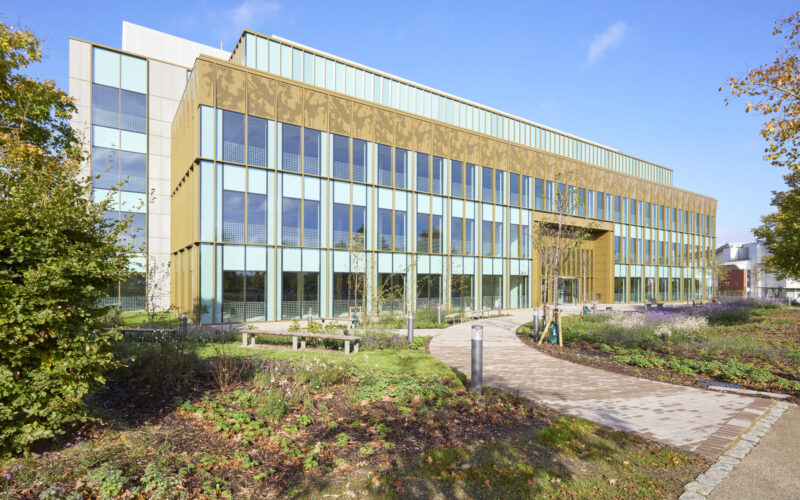 Exterior of a low rise office building with lots of windows and green planting in the foreground