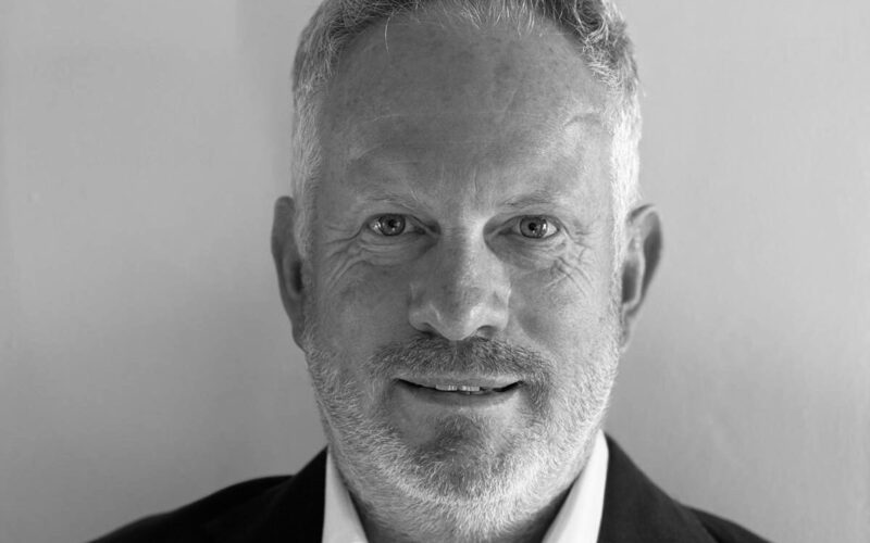 Black and white picture of Ivan Scott who is wearing a dark suit, a white shirt and no tie