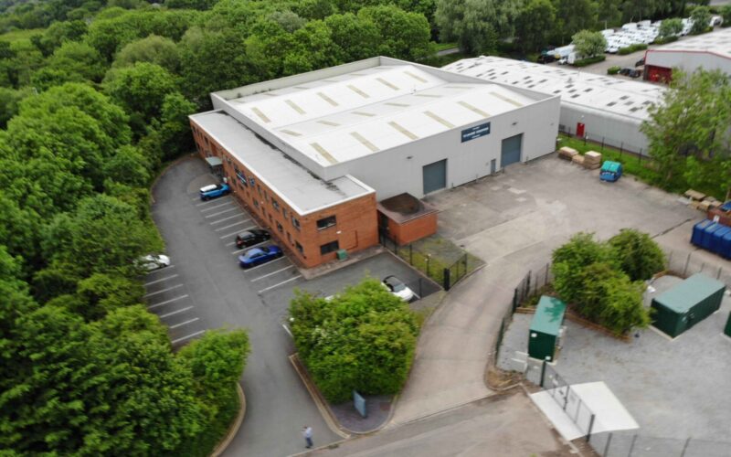 Aerial view of an industrial building with a large wooded area to the side and the rear