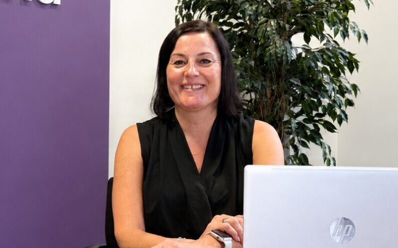 A woman with dark hair and a black shirt sat behind a desk with a computer in front of her