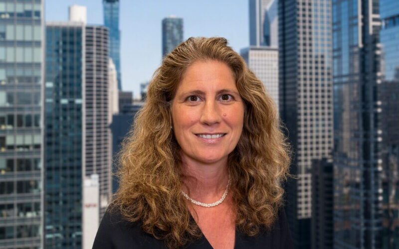 A woman with wavy long hair wearing a black shirt with skyscrapers in the background