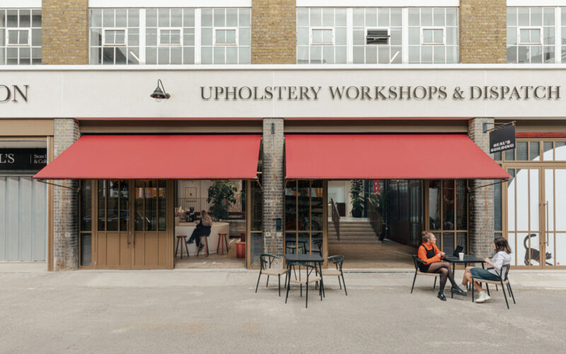 Exterior of the iconic Heal's building in London with people sat outside the entrance which has large red blinds