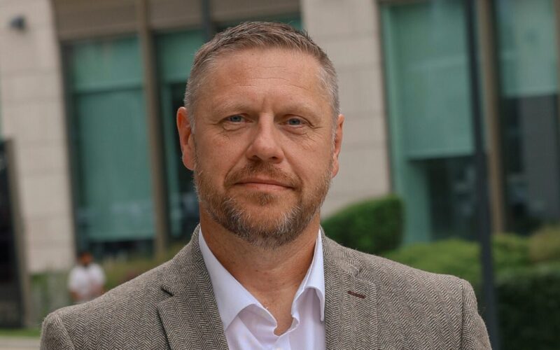 A white male with a short beard and short hair wearing a jacket and white shirt