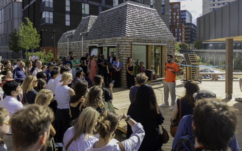 A man wearing a bright shirt stood in front of a crowd of people at a new neighbourhood garden at King's Cross
