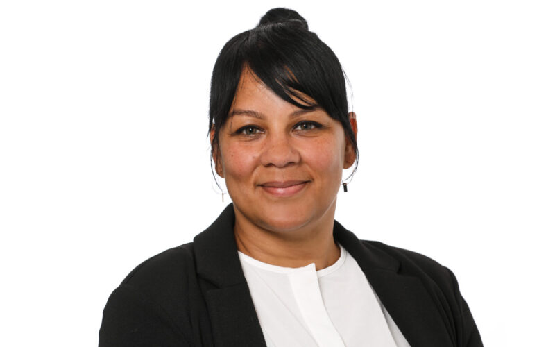 A smiling woman with black hair wearing a dark jacket and a white shirt