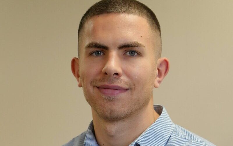 Patrick Swallow has short hair and is wearing a blue collared shirt