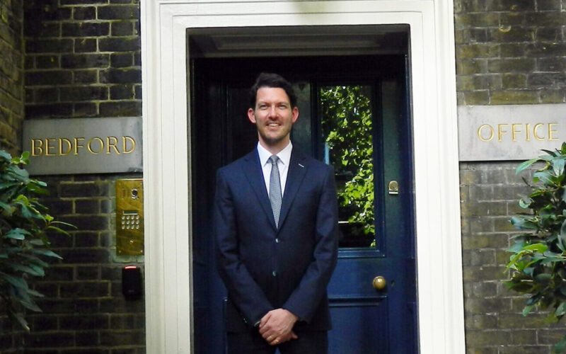 A man wearing a dark suit stood in front of an ornate doorway