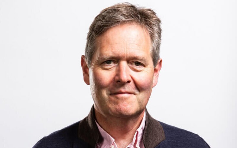 A white man wearing a dark jacket and a light shirt