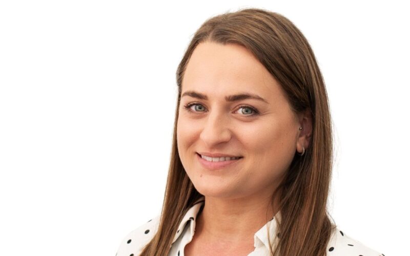 A female with long brown hair wearing a white polka dot shirt