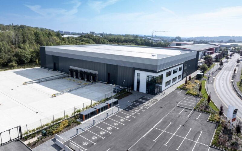 Aerial view of a modern industrial building with a large goods yard to the side and car parking out front