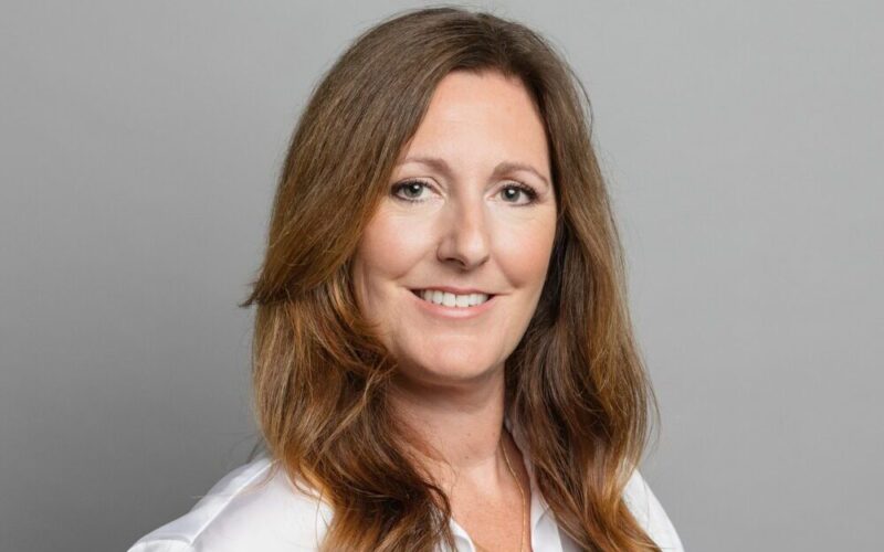 A middle-aged woman with long brown hair wearing a white satin shirt